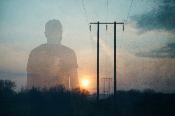 A double exposure of an atmospheric half transparent man looking at the sunset. Next to telegraph poles in the countryside.  - Fotoğraf, Görsel