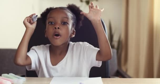 Webkamera pohled malé Afro americké dítě roztomilé dívka mluví kreslí s jasnými markery dělá obrázek na papíře s barevnými markery komentáře na tvůrčí proces záběry video pro blog, domácí volnočasové koncepce - Záběry, video