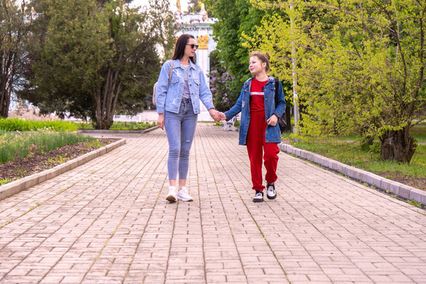 Äiti ja teini-ikäinen tytär kävelemässä puistossa, pitämässä kädestä, onnellinen nuori valkoihoinen nainen, jolla on pitkät hiukset ja teini-ikäinen tyttö, joka hengailee kaupungissa, elämäntapa perheessä. - Valokuva, kuva