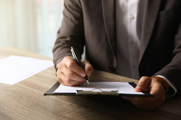 Businessman signing document at table indoors, closeup - Photo, image