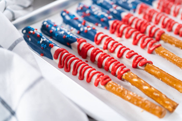 Homemade chocolate-covered pretzel rods decorated like the American flag drying on a baking sheet lined with parchment paper. - Photo, Image