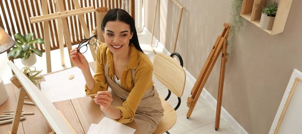 Young woman drawing on easel with pencil at table indoors, above view. Banner design - Foto, Imagen