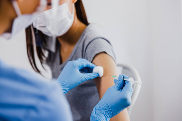 Закройте азиатскую женщину-врача, держащую шприц и использующую хлопок, прежде чем делать инъекции пациентам в медицинской маске. Ковид-19 или коронавирусная вакцина - Фото, изображение