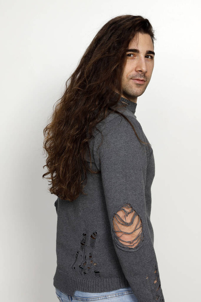Привабливий молодий хлопець з дуже довгим кучерявим волоссям позує в студії. Стиль, тенденції, концепція моди
. - Фото, зображення