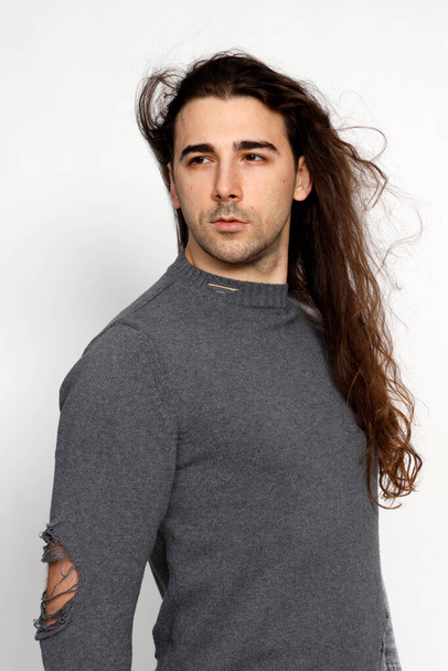 Atraktivní mladík s velmi dlouhými kudrnatými vlasy pózuje ve studiu. Styl, trendy, módní koncept. - Fotografie, Obrázek