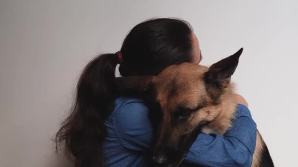 Young pretty girl of Caucasian European appearance hugs her German Shepherd dog. Woman and dog on white background sit close and love each other. Warm relationship between person and pet. - Video, Çekim