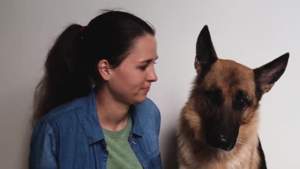Young pretty girl of Caucasian European appearance kisses her German Shepherd dog. Woman and dog on white background sit close and love each other. Warm relationship between person and pet. - Video, Çekim
