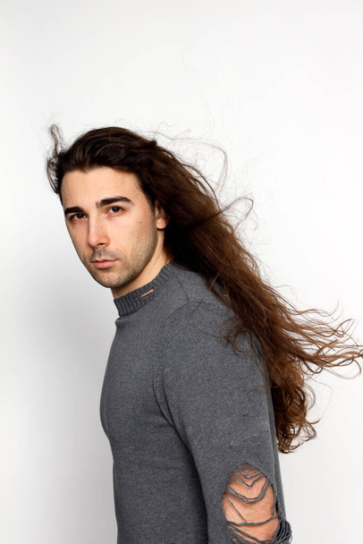 Attractive young guy with very long curly hair is posing in studio. Style, trends, fashion concept. - Foto, Imagem