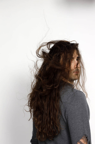 Jeune homme attrayant avec de très longs cheveux bouclés pose en studio. Style, tendances, concept de mode. - Photo, image