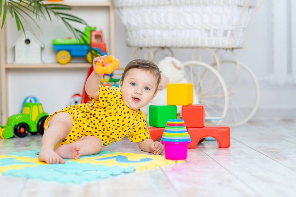 chlapeček si hraje v dětském pokoji ve žlutém obleku s pestrobarevnými hračkami - Fotografie, Obrázek