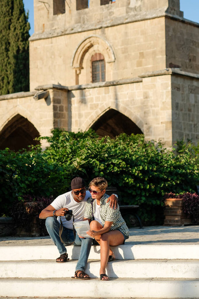 Eine multiethnische Gruppe von Freunden spaziert durch die Altstadt. Gemischtes Paar schaut auf Landkarte, redet und lacht. Viertel mit altem Stil im Hintergrund. Reisekonzepte für Lifestyle und Freundschaft. - Foto, Bild