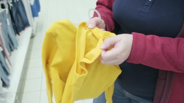 Zwangere vrouw kiest een gele kleding - lijfje voor een baby in een winkel te kopen - Video
