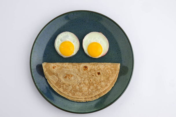 Chappati, une nourriture saine faite de farine de blé et les yeux sont faits d'œufs à moitié cuits et il est disposé dans une assiette en céramique aqua rustique avec fond blanc. - Photo, image