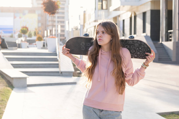 Beautiful ginger teenage girl holding skateboard in her hands. Lifestyle in the city. - Φωτογραφία, εικόνα