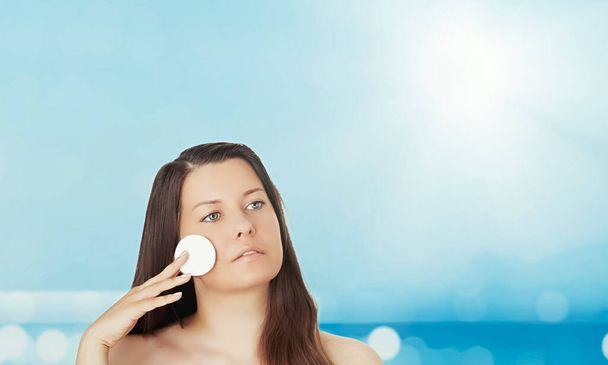 Huidverzorging en zonbescherming in de zomer. Portret van een prachtige jonge zongebruinde vrouw, blauwe zee en lucht op achtergrond, schoonheid, wellness en reisconcept - Foto, afbeelding