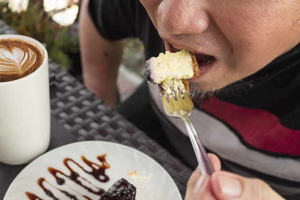 Ένας άνθρωπος τρώει cheesecake βατόμουρο σε μια al fresco ή υπαίθρια καφετέρια ή εστιατόριο. - Φωτογραφία, εικόνα