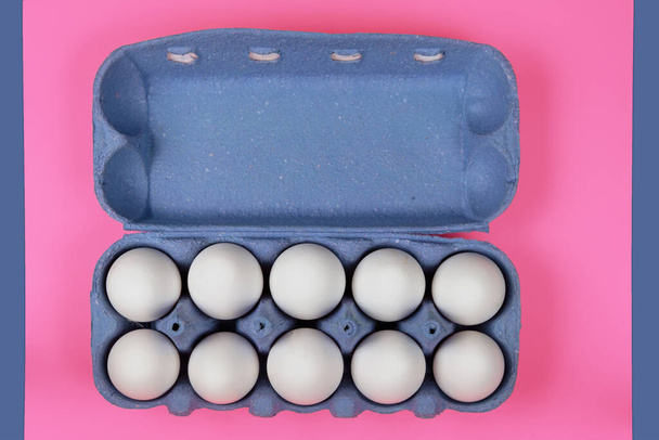 Huevos de pollo blancos en una bandeja de papel sobre una superficie rosa - Foto, imagen