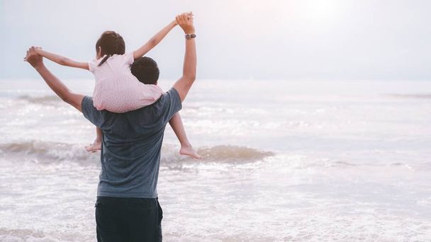 幼い娘がパパの首に乗ってる。父親と娘がビーチに立っている。父の日と家族の余暇の概念 - 写真・画像