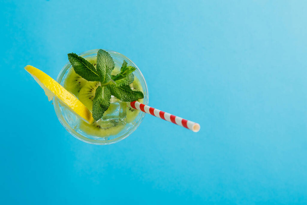 Kiwi cocktail decorated with lemon and mint in a glass on a napkin on a blue background top view. Horizontal photo - Fotoğraf, Görsel