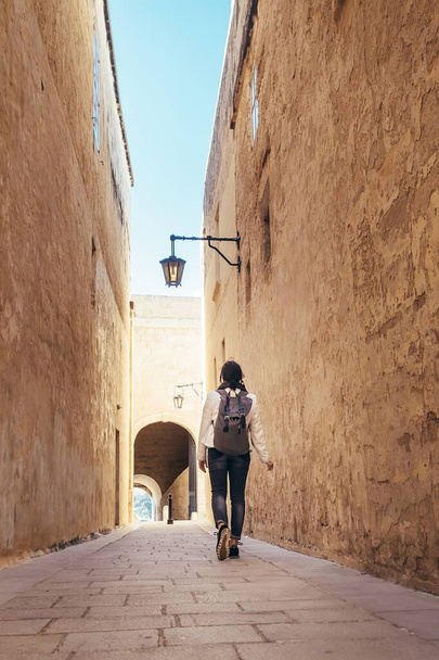 Female traveling alone on the Malta island. Tourist walking by the narrow ancient medieval Mdina streets with a city backpack and enjoying an historical place. - Photo, Image