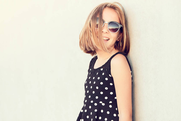 Teini-ikäisen argentiinalaisen tytön muotokuva, jolla on aurinkolasit ja pilkkumekko, eristettynä sementtitaustan päälle. Kopioi tila. - Valokuva, kuva