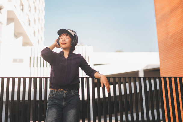 Happy young asian woman listening to music and having fun with headphones on the street. - Foto, Bild