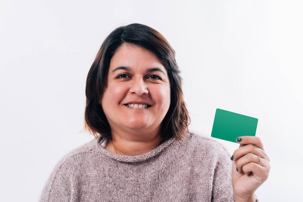 Portrait d'une femme qui sourit et gèle avec sa main une carte de crédit verte en fond blanc. Concept de shopping sur Internet. Espace de copie - Photo, image