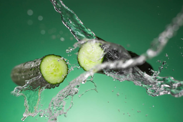 Pepino fresco y salpicaduras de agua sobre fondo verde - Foto, Imagen