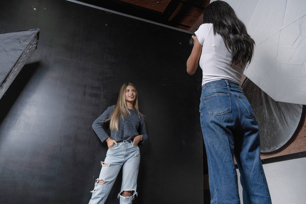 Horizontal portrait of a photo session of a model and a woman photographer in a photography studio, black background. - Photo, Image