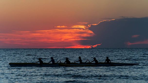 Roeien bemanning in silhouet op water tegen pastel zonsondergang hemel - Foto, afbeelding