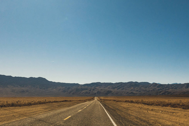 Route du désert menant à l'horizon contre un ciel bleu clair et des montagnes - Photo, image