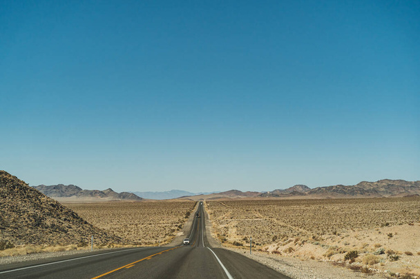 Desert highway road leading to the horizon against clear blue sky and mountains - Photo, Image