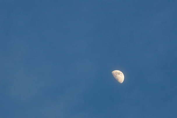 The moon is seen as a half-moon in the evening sky with faint clouds in the surrounding negative copy space. - Photo, Image