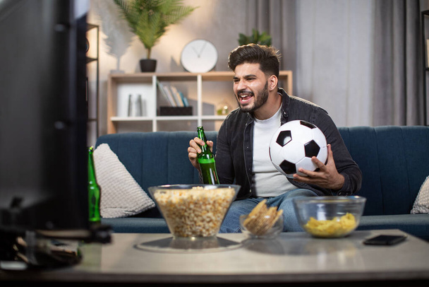 Ενθουσιασμένος Ινδός με πατάτες και μπύρα βλέποντας ποδόσφαιρο στην τηλεόραση - Φωτογραφία, εικόνα