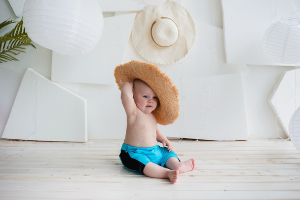 gyerek nyári fiú kék rövidnadrágban és egy szalma kalap ül egy fehér háttér hely szöveges - Fotó, kép
