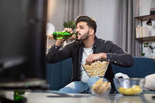 Indian guy drinking beer while watching soccer match at home - 写真・画像