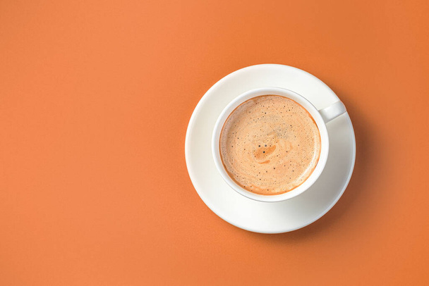 Coffee in a white cup and saucer on a terracotta background. Morning cappuccino. Top view, copy space. - Photo, Image