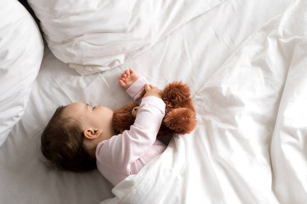 Authentic portrait cute caucasian little infant chubby baby girl or boy in pink sleep with teddy bear on white bed. child resting at lunchtime. care, Sleeping kid, Childhood, Parenthood, life concept - Foto, imagen