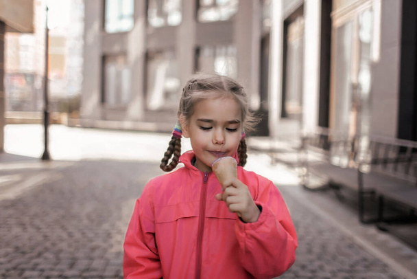 Όμορφο κορίτσι τρώει παγωτό στο δρόμο πάνω από αστικό υπόβαθρο, αστείο παιδί καραμέλα, έξω από τον τρόπο ζωής - Φωτογραφία, εικόνα