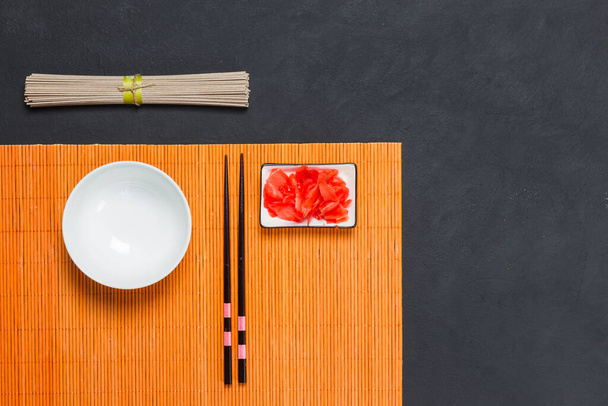 Koncept vaření japonských pohankových nudlí soba. Soba se podává s omáčkou, vývarem, používá se v salátech, poka, horké maso a vegetariánská jídla. Hromada nudlí, zázvoru, hůlek a misky polévky na černém pozadí - Fotografie, Obrázek