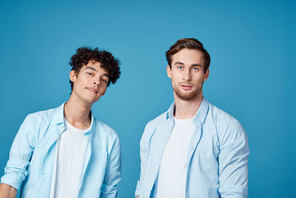 two friends in identical shirts and a t-shirt gesturing with their hands on a blue background - Fotoğraf, Görsel