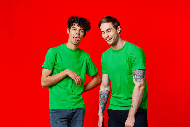 dos amigos en camisetas verdes están de pie junto a la lata con sus manos emociones - Foto, Imagen