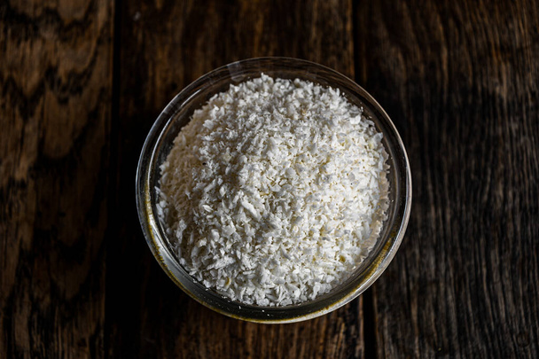 Coconut shavings in a glass dish, on a wooden table. - Photo, Image