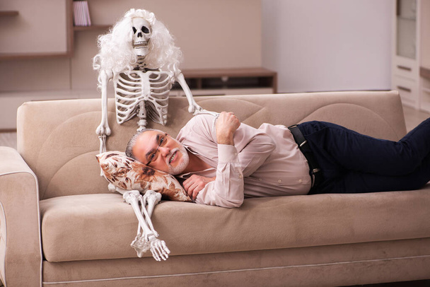 Old man sitting on the sofa with the female skeleton - Foto, Bild