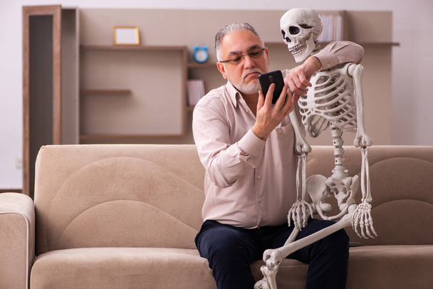 Alter Mann sitzt auf dem Sofa mit dem weiblichen Skelett - Foto, Bild