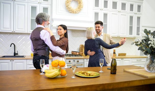 Two multigenerational couples dancing in kitchen when celebrating birthday - Photo, Image