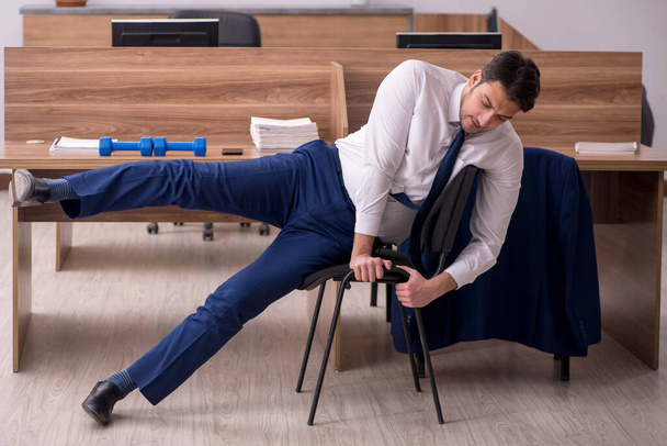 Молодой бизнесмен делает спортивные упражнения на рабочем месте - Фото, изображение