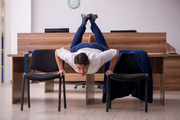 Young businessman employee doing sport exercises at workplace - Photo, Image