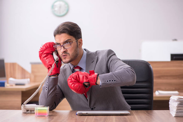 Young male employee wearing boxing gloves at workplace - Photo, Image