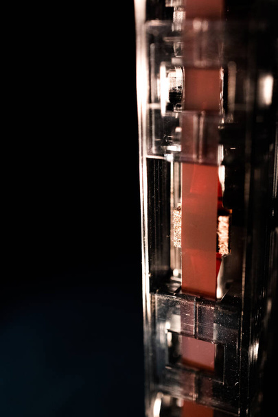 Macro Κλείσιμο της κόκκινης ταινίας στο κάτω μέρος της κατακόρυφης κασέτας που απομονώνεται στο μαύρο φόντο - Φωτογραφία, εικόνα